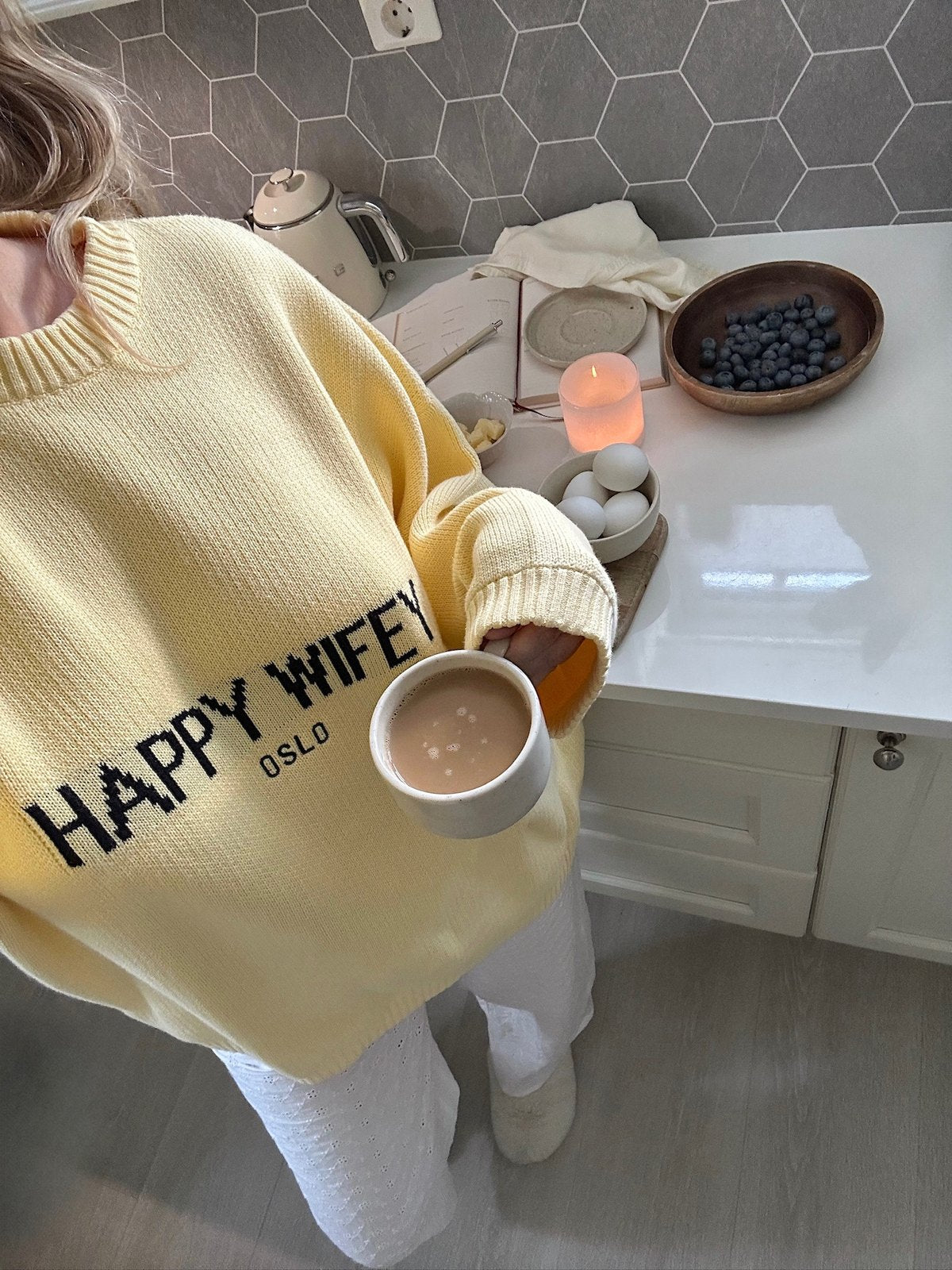 Enjoying a warm drink at home in a Happy Wifey knit sweater